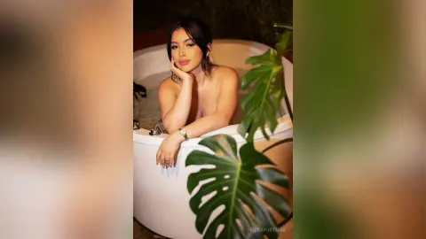 VickyPortman poses in a white bathtub, looking at the camera with her hand resting on her neck.