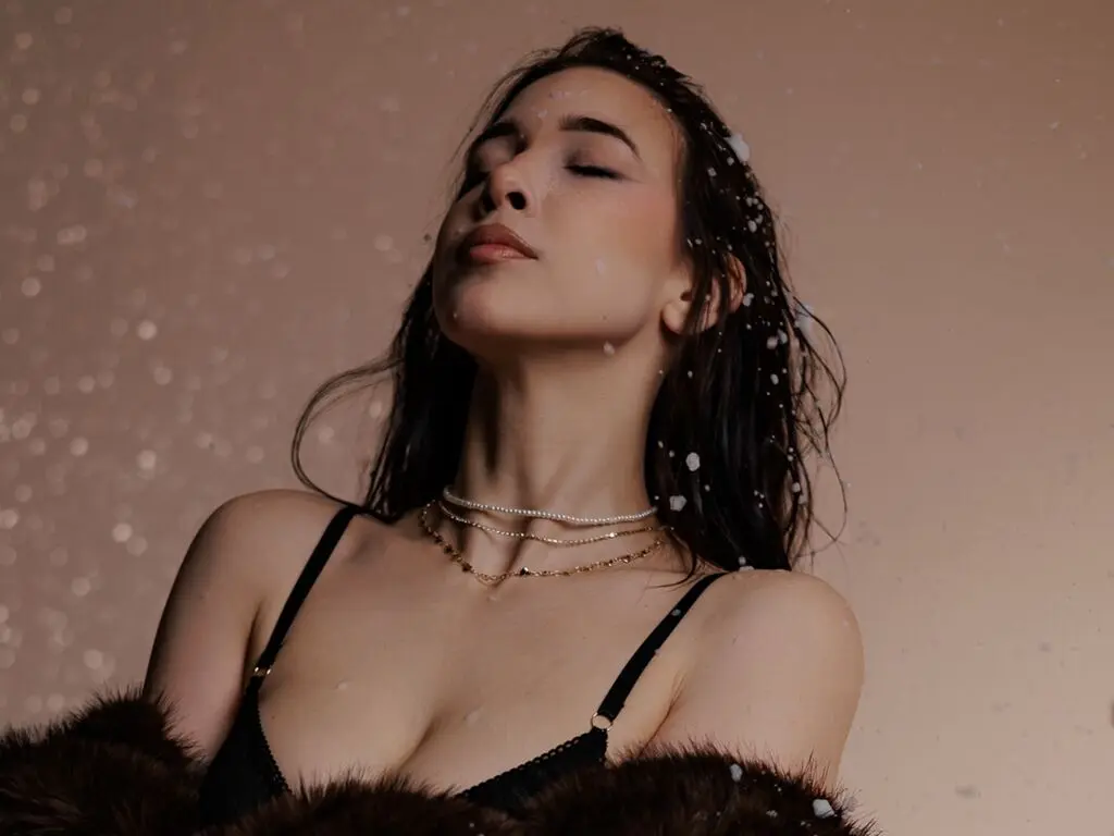 Serene woman in a black lace bra and faux fur coat posing against a dreamy, sparkling bokeh background.