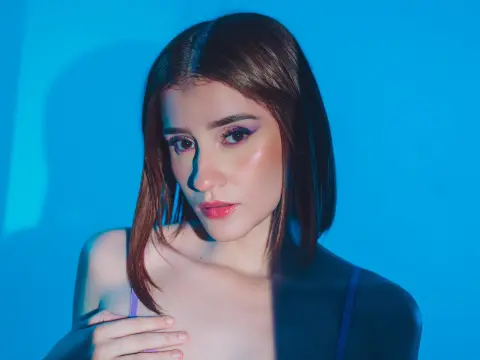 Young woman with straight brown hair in a moody blue studio setting wearing a dark strap top.