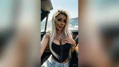 Blonde woman in a black corset top sitting in a convertible car by the ocean on a sunny day.