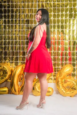Smiling woman in a red cocktail dress posing by gold balloons against a shimmering sequin backdrop.