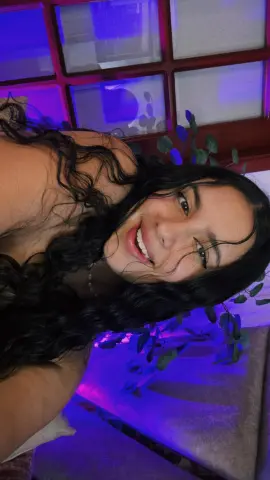 Smiling young woman with long curly hair posing in a room with moody purple ambient lighting.