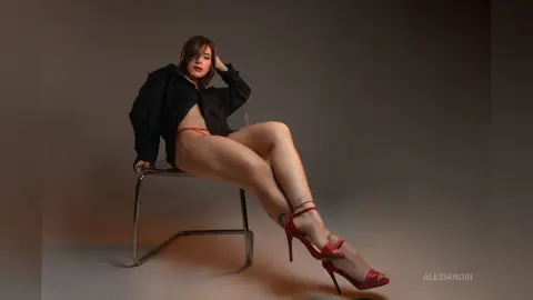 Young woman in a black shirt and red lingerie sitting on a chair in a moody studio setting.