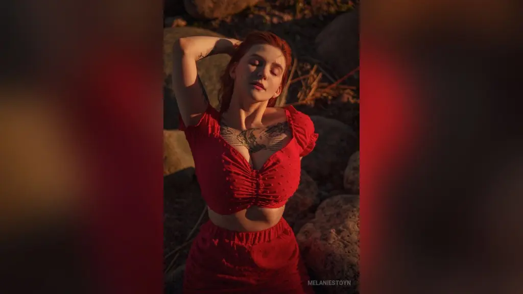 MelanieStoyn โ Redheaded woman in a red crop top posing in warm sunset lighting amidst rocky outdoor terrain.