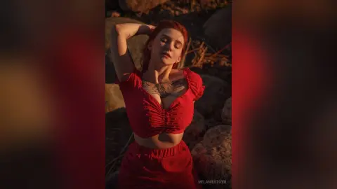Redheaded woman in a red crop top posing in warm sunset lighting amidst rocky outdoor terrain.