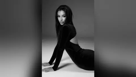 Elegant woman in a sleek black long-sleeve dress posing gracefully in a minimalist studio setting.