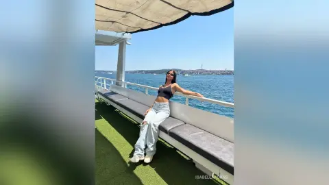 Woman in black crop top and light jeans relaxing on a boat deck under a sunny blue sky.