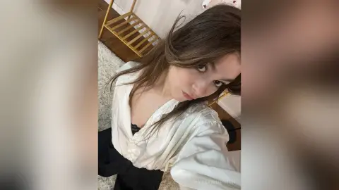 Young woman in a white satin robe relaxing in a bright, cozy bedroom setting.