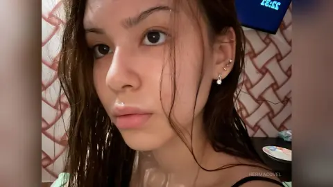Close-up portrait of a young woman with wet hair and silver earrings in a warm indoor setting.