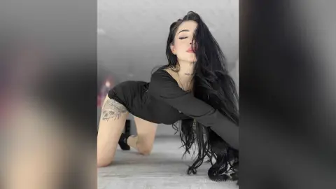 Young woman with long dark hair in a black long-sleeve bodysuit posing gracefully on a white floor.