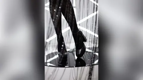 Elegant woman in black patterned tights and high heels standing against a shimmering light backdrop.