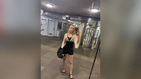 KeilaTouchton takes a mirror selfie in a black romper and white lace shrug, standing in a subway station.