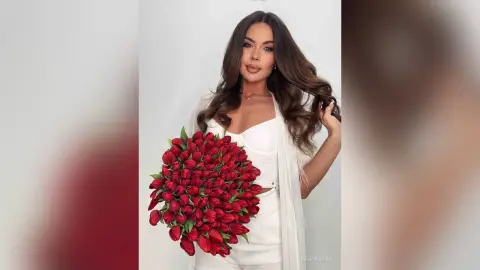 Elegant woman in a white outfit holding a large bouquet of red tulips against a clean studio background.