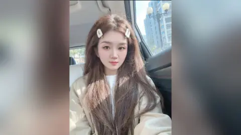 Young woman with long brown hair and white hair clips smiling in a car during a bright day.