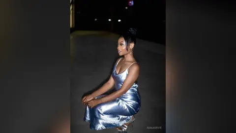Elegant woman in a shimmering silver satin slip dress sitting outdoors at night under soft lighting.