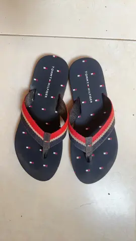 Pair of navy blue Tommy Hilfiger flip flops with red and white striped fabric straps on a light floor.