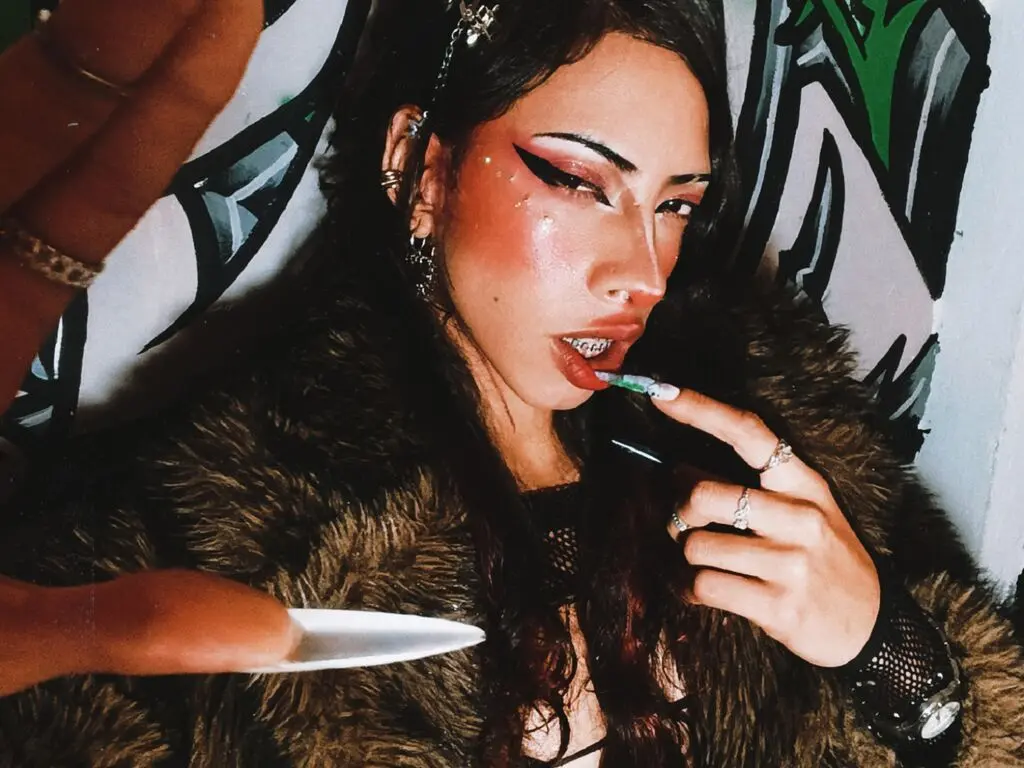 Edgy woman with winged eyeliner and faux fur coat posing in front of graffiti art.