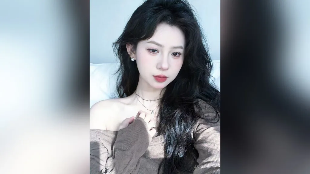 AnnLinMei — AnnLinMei with long wavy black hair poses in a brown off-the-shoulder top.