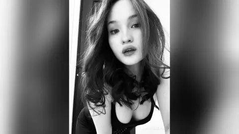 Portrait of a young woman in a black top with a moody, cinematic black and white aesthetic.