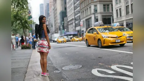 Stylish woman in a blue top and patterned skirt with black wings standing on a busy New York City street.