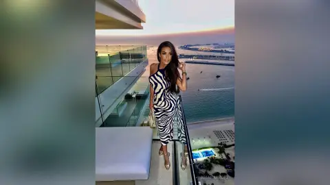 Elegant woman in a black and white zebra print dress standing on a luxury balcony at sunset.
