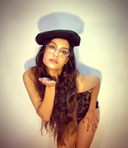 Glamorous woman in a black beret and glasses blowing a kiss against a neutral studio background.