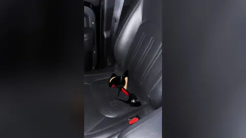 Hailey's black high-heeled pumps resting on a black leather car seat.