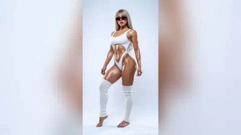 NatashaCastello poses in a white cutout bodysuit and tall white socks against a plain background.