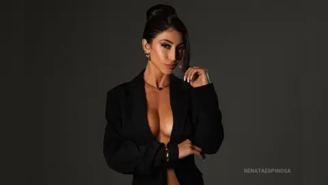 Elegant woman in a black blazer and gold jewelry posing against a dark studio background with a sophisticated mood.