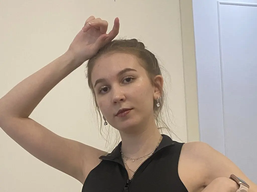 Young woman in a black sleeveless top and silver jewelry posing indoors with a relaxed mood.