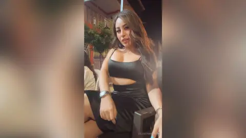 Glamorous woman in a black cutout cocktail dress posing at an outdoor evening event.