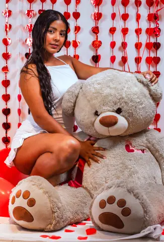 Woman in a white summer dress sitting with a giant teddy bear against a romantic red heart backdrop.