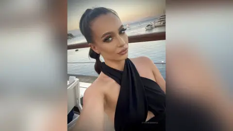 Glamorous woman in a black halter dress posing on a balcony overlooking the ocean at sunset.