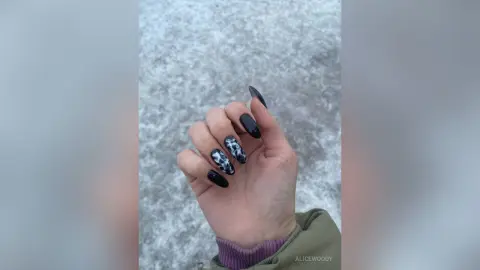 Close-up of a hand with trendy black and white marble patterned manicured nails against a textured grey background.