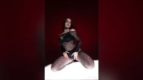 Young woman in a black lace bodysuit posing against a dark red background with a moody, cinematic aesthetic.