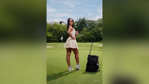 Stylish woman in a white tennis dress holding a golf club on a sunny green golf course.