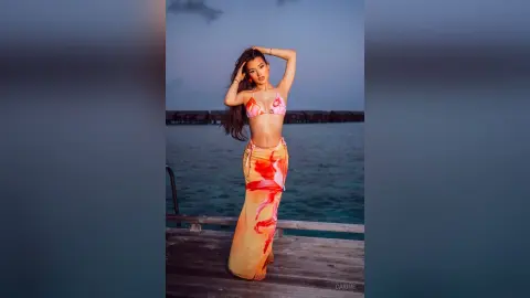 Carine poses on a wooden pier wearing a red and white patterned bikini top and a matching long skirt.