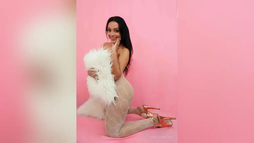 RenataBrown — Smiling woman in a white faux fur coat and patterned tights posing against a pink background.