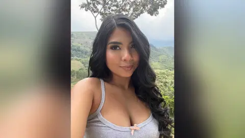 Smiling young woman in a grey ribbed tank top enjoying a scenic mountain view on a cloudy day.
