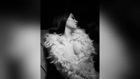 Glamorous woman in a white feathered outfit posing elegantly in a moody black and white portrait.