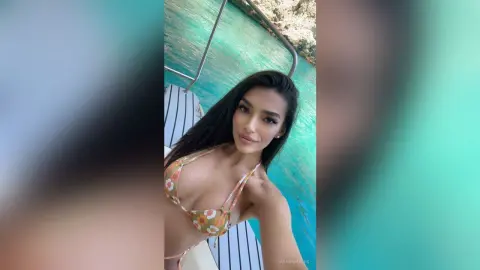 Smiling brunette woman in a floral bikini relaxing on a boat in turquoise tropical ocean water.