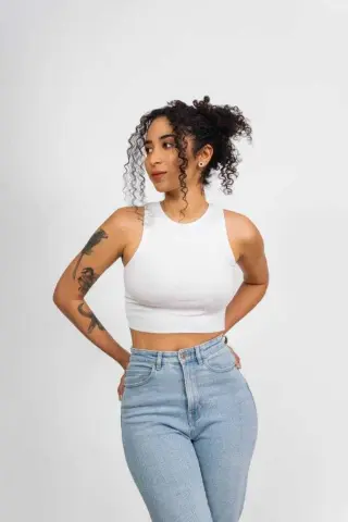Young woman with curly hair wearing a white crop top and light blue jeans against a white background.