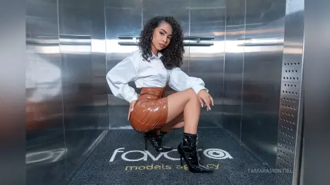 Stylish woman in a white blouse and brown leather skirt posing confidently in a modern elevator.