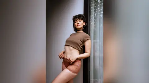 IveteDurand poses in a brown crop top and sheer lace panties, showing her midriff and hips while leaning against a doorframe.