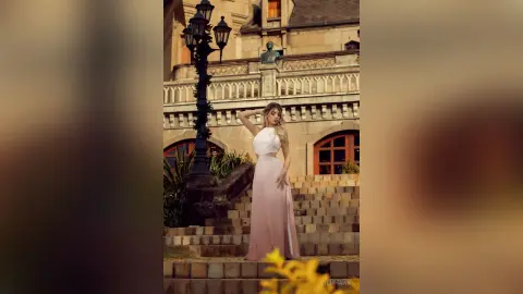 Elegant woman in a white sleeveless maxi dress posing on stone stairs before a classic European building.