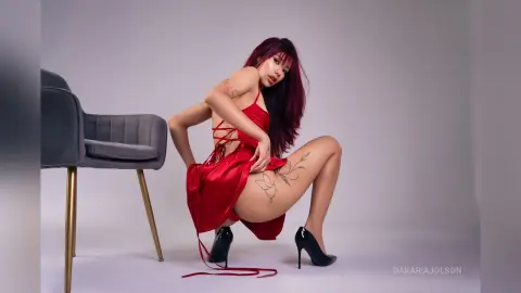 Woman with red hair in a red satin dress posing in a studio setting with a moody, elegant vibe.