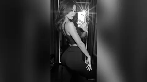 Slim woman in black athletic crop top and leggings taking a moody black and white mirror selfie.