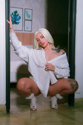 Blonde woman in an oversized white shirt and lace socks squatting in a doorway with a moody, aesthetic vibe.