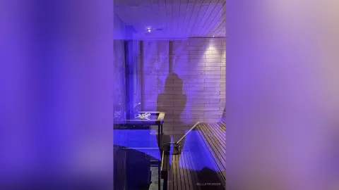 Shadow of a person in a modern spa room with blue lighting and wooden slats creating a moody atmosphere.