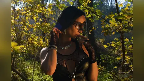 Mysterious woman in a black lace outfit and masquerade mask posing in a sunlit autumn forest.